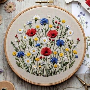 May include: A hand-stitched embroidery hoop featuring a vibrant floral design. The artwork showcases red poppies, white daisies, blue cornflowers, and yellow wildflowers, all set against a neutral fabric background. The wooden hoop provides a natural frame for the botanical scene.