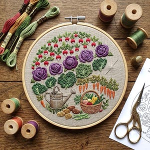 Peut inclure: Un tambour à broder présentant une scène de jardin avec des radis, des choux violets, du chou frisé, des carottes, un arrosoir et un panier de légumes brodés. Le kit comprend des fils à broder colorés, des bobines en bois, un dé et des ciseaux.