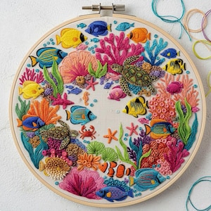 May include: A colorful embroidery hoop featuring an underwater scene. The design includes various fish, coral, sea turtles, and other marine life. The artwork is created with vibrant threads in shades of blue, yellow, orange, pink, and green, creating a detailed and textured effect.