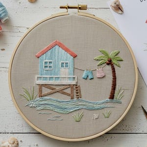 May include: Embroidered beach scene in a wooden hoop. A blue beach house with a red roof sits on stilts, with a palm tree and clothesline. The scene includes embroidered waves, grass, and a ladder. The hoop is approximately 8 inches in diameter.