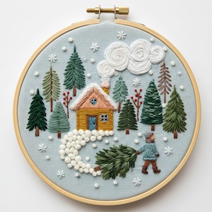 May include: Embroidered winter scene in a wooden hoop. A yellow cabin with a snow-covered roof is surrounded by green trees and falling snowflakes. A person pulls a Christmas tree through the snow. The background is light blue.