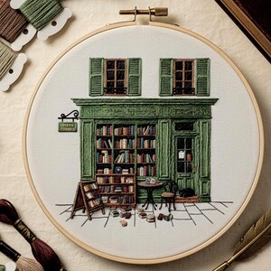 以下が含まれることがあります： 刺繍されたフレームアート作品で、趣のある本屋を詳細に描写しています。デザインは、本棚、窓、ドアを備えた緑色のファサードを特徴とし、すべて丁寧にステッチされています。本の入り口の周りに散らばっており、小さな黒猫がドアの近くで休んでいます。