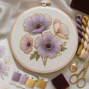 May include: An embroidery hoop with a floral design of purple and pink flowers, outlined in gold thread. Embroidery floss in various colours, gold scissors, and a small velvet box are also visible.