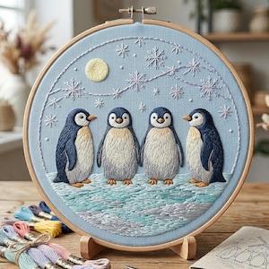 Puede incluir: Arte bordado en un aro de madera, que representa cuatro pingüinos sobre un fondo azul claro con copos de nieve y una luna amarilla. Los pingüinos tienen cuerpos blancos y negros y están sobre un paisaje nevado. El bordado es detallado.