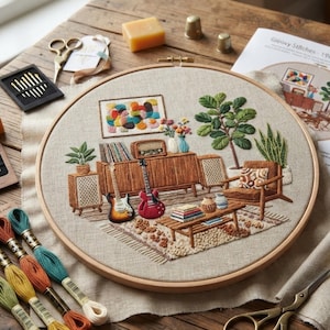 May include: A round wooden embroidery hoop containing a detailed needlepoint scene of a living room with a mid-century sideboard, two electric guitars, a potted plant, a chair, and a coffee table with books, all stitched on beige fabric.