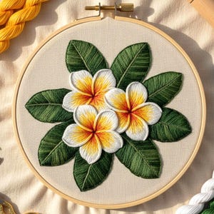 May include: Embroidered floral hoop art showing three white and yellow plumeria flowers with green leaves. The embroidery is on a beige fabric, held in a wooden hoop with a brass clasp. Yellow thread is visible, with the hoop measuring approximately 20 cm in diameter.