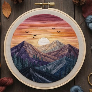 May include: Hand-stitched embroidery art in a round hoop. The artwork depicts a sunset over a mountain range, with a gradient of colors from deep purple to orange and yellow. The sun is a white circle, and birds are flying in the sky.