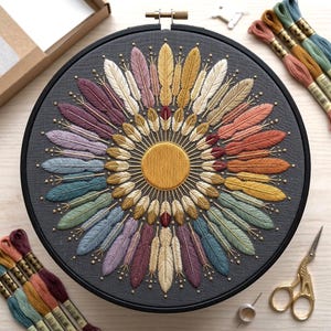 May include: A circular embroidery hoop containing a dark gray fabric with a central golden yellow circle surrounded by a radial pattern of embroidered feathers in various colors including pink, blue, green, and orange, with small gold beads.