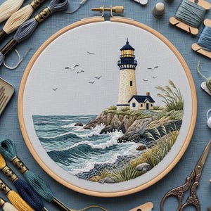 May include: A circular wooden embroidery hoop containing a detailed needlepoint scene of a lighthouse on a rocky cliff overlooking a blue ocean with white waves, green coastal grass, and several birds flying in the sky above the structure.