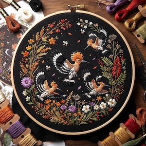 May include: A circular wooden embroidery hoop containing black fabric with a detailed needlepoint design of three hoopoe birds in flight, surrounded by a colorful wreath of various wildflowers, wheat stalks, and small bees.