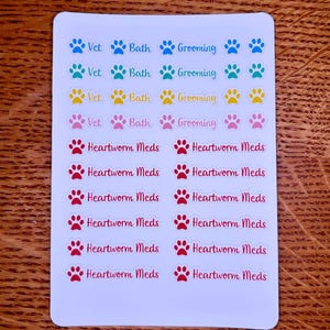 May include: A sheet of colorful pet care stickers. The top section features paw prints with the words "Vet," "Bath," and "Grooming." The bottom section has red paw prints with the words "Heartworm Meds."