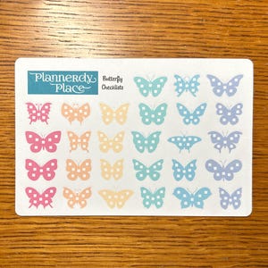 May include: A sheet of planner stickers featuring colorful butterfly designs in pink, orange, yellow, teal, and blue. The stickers are arranged in rows and columns. The sheet has the text "Plannerdy Place" and "Butterfly Checklists".