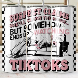 Puede incluir: Un vaso blanco con un patrón de cuadros blanco y negro. El vaso tiene un gráfico rosa y negro que dice "Suspect Claims She'll Clean The House... But Somehow Ends Up Watching TikToks". El gráfico también incluye una caricatura de una persona en un sofá mirando un teléfono.