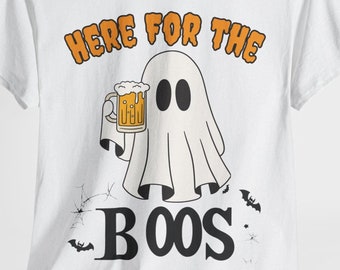 May include: White t-shirt with a Halloween-themed graphic. The design features a cartoon ghost holding a beer mug, with the text "HERE FOR THE BOOS" in orange and black. Bats and spiderwebs are also included in the design.