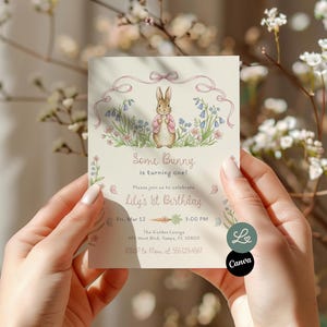 Op de afbeelding: Een crèmekleurige verjaardagsuitnodigingskaart met een aquarelillustratie van een konijn in een roze jasje tussen bloemen. De tekst luidt "Some Bunny is turning one!" en "Lily's 1st Birthday". De kaart wordt door een persoon vastgehouden.