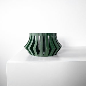 May include: A dark green, geometric planter with a wide, round base and a narrow top. The planter is made of a lightweight material and has a modern design.