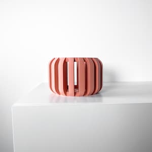 May include: A pink, cylindrical planter with a geometric design. The planter is made of wood and has a series of vertical slats.