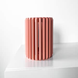 May include: A coral pink cylindrical planter with vertical slats. The planter is made of a smooth, solid material and has a modern design.
