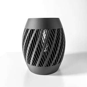 May include: A black, cylindrical, decorative planter with a geometric, lattice-like design. The planter is made of a solid material and has a smooth, matte finish.