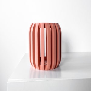 May include: A pink cylindrical planter with a slatted design. The planter is made of wood and has a smooth finish.