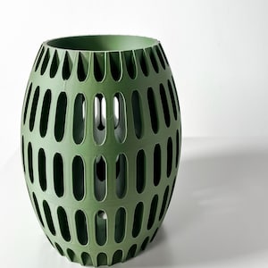 May include: A green, round, decorative planter with a geometric pattern of oval cutouts. The planter is made of a smooth, textured material.