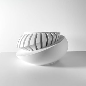 May include: White ceramic planter with a geometric design. The planter has a rounded shape and a series of vertical ridges around the top.