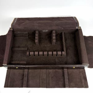 May include: Open brown silverware storage case with a zippered top. The interior is lined with a dark brown fabric and features compartments for various utensils. The case is designed to protect and organize flatware.