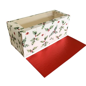 May include: A rectangular gift box decorated with a holly and berry pattern on a white backdrop. The box is open, showing a beige interior. A separate, shiny red rectangle is placed beside the box.