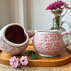 Puede incluir: Dos tazas de cerámica rosa y blanca con un diseño floral. Las tazas están sobre una bandeja de madera con una ramita de flores rosas.