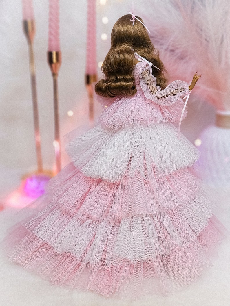 May include: A pink and white tulle dress with a layered skirt and a sheer bodice. The dress is decorated with small white dots.