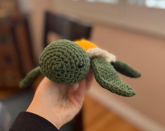 May include: A crocheted green turtle toy with a yellow and white shell. The turtle has black eyes and a small mouth.