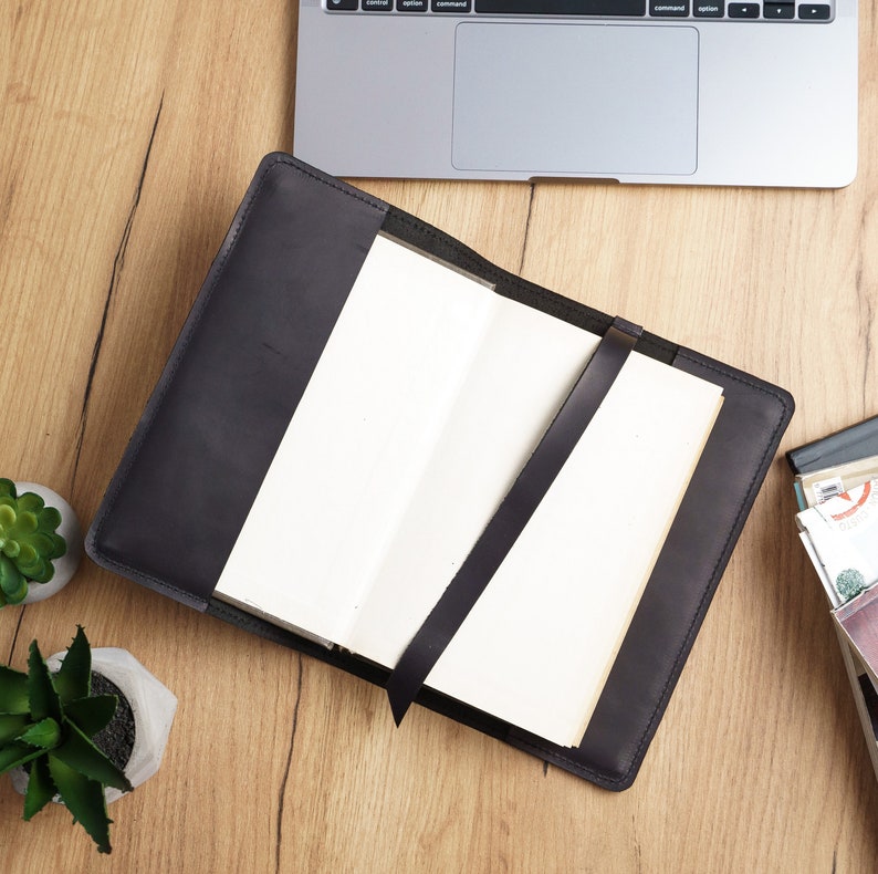 May include: A black leather notebook cover with a blank notebook inside. The cover has a brown leather strap.