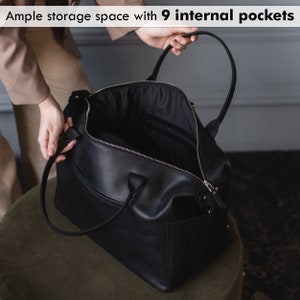 K&ouml;nnte beinhalten: Eine schwarze Leder-Reisetasche mit Rei&szlig;verschluss und einem oberen Tragegriff. Die Tasche ist ge&ouml;ffnet und zeigt das Innenfutter und neun Innentaschen.