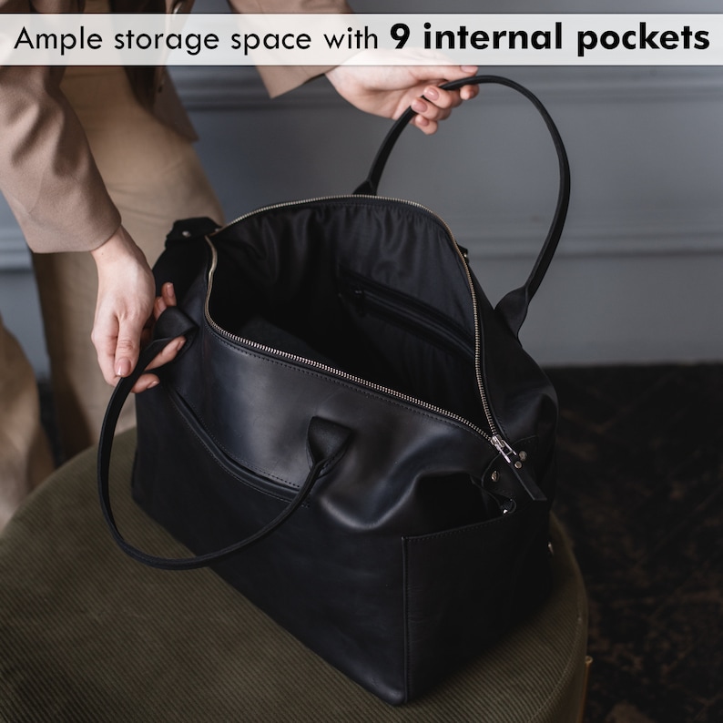 K&ouml;nnte beinhalten: Eine schwarze Leder-Reisetasche mit Rei&szlig;verschluss und einem oberen Tragegriff. Die Tasche ist ge&ouml;ffnet und zeigt das Innenfutter und neun Innentaschen.