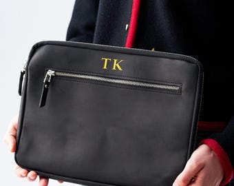 Può includere: Custodia per laptop in pelle nera con cerniera dorata e le iniziali "TK" ricamate in oro sul davanti.