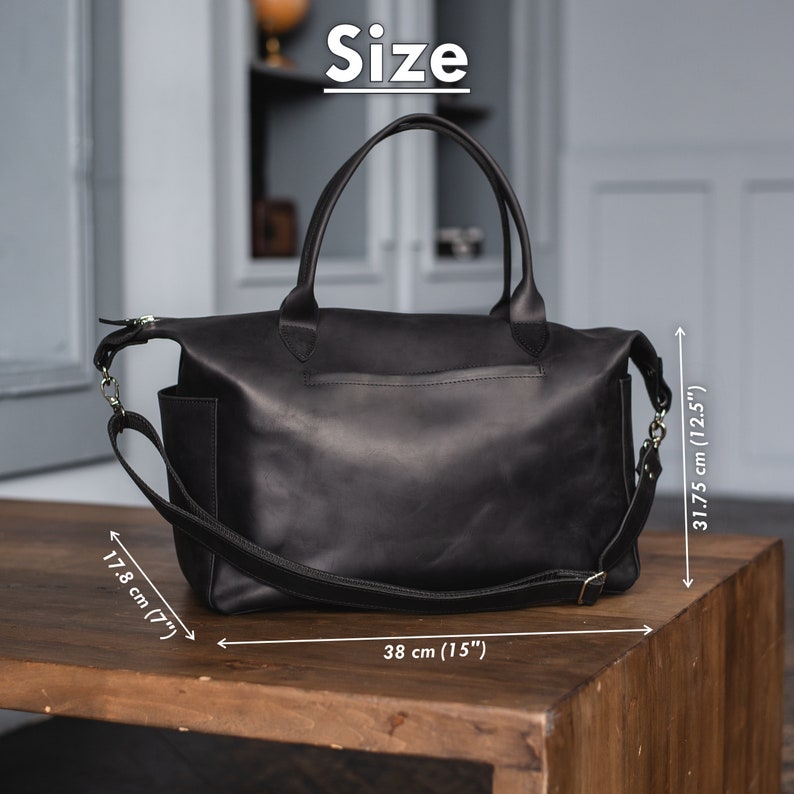 K&ouml;nnte beinhalten: Schwarze Ledertasche mit einem oberen Henkel und einem langen Schultergurt. Die Tasche misst 38 cm in der Breite, 31,75 cm in der H&ouml;he und 17,8 cm in der Tiefe.