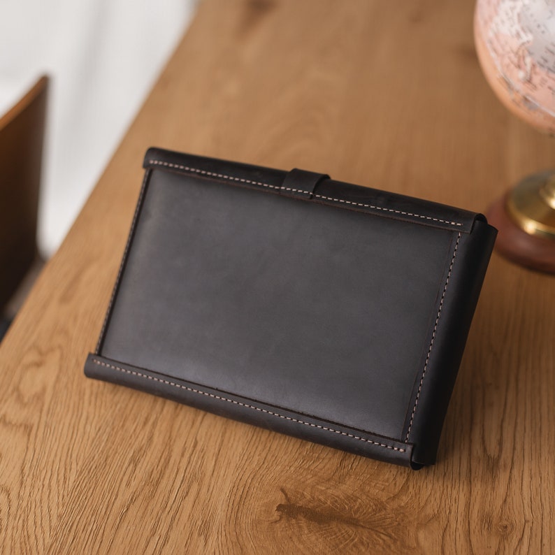 May include: A dark brown leather wallet with a stitched edge. The wallet is closed and lying on a wooden surface.