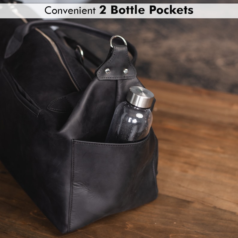 K&ouml;nnte beinhalten: Schwarze Leder-Reisetasche mit zwei Seitentaschen, eine mit einer Wasserflasche. Der Text "Convenient 2 Bottle Pockets" ist oben im Bild sichtbar.