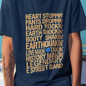 Puede incluir: Una camiseta azul marino con texto dorado que dice "HEART STOPPIN' PANTS DROPPIN' HARD ROCKIN' EARTH SHOCKIN' BOOTY SHAKIN' EARTHQUAKIN' LOVE MAKIN' TAKIN' HISTORY MAKIN' LEGENDARY E STREET BAND"