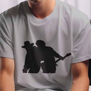 Op de afbeelding: Een man draagt een lichtgrijs T-shirt met een zwart silhouet van twee mensen die muziek maken. Het shirt heeft een ronde hals en korte mouwen.