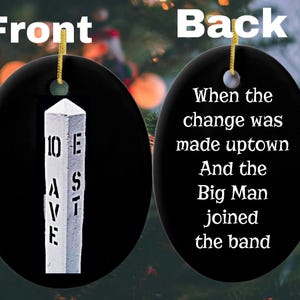 May include: An oval black ceramic ornament with a gold hanging string. The front features a white street sign post labeled 10 AVE E ST. The back displays white text reading: When the change was made uptown And the Big Man joined the band.