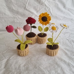 May include: Four crocheted potted plants with different flowers. The plants are a pink and red tulip, a red rose, a yellow sunflower, and a white daisy.