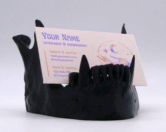 May include: Black skull-shaped business card holder with a white business card that reads "YOUR NAME ASTROLOGIST & NUMEROLOGIST WEBSITE & SOCIALS reallygreatsite.com @reallygreatsite PHONE & ADDRESS +123-456-789 123 Anywh"