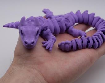 Może przedstawiać: Fioletowa, 3D-drukowana, artykułowana figurka smoka z segmentowanym ogonem. Smok ma szczegółową głowę z małym pyskiem i dużymi oczami.