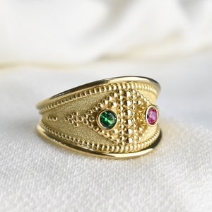May include: A gold ring with a textured band and two gemstones. The larger gemstone is green and the smaller gemstone is red.