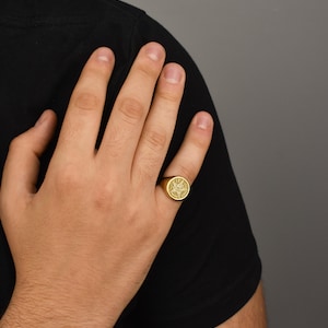May include: A gold signet ring with a detailed design on the face.