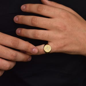 K&ouml;nnte beinhalten: Ein goldener Siegelring mit einem detaillierten Design auf der Vorderseite.