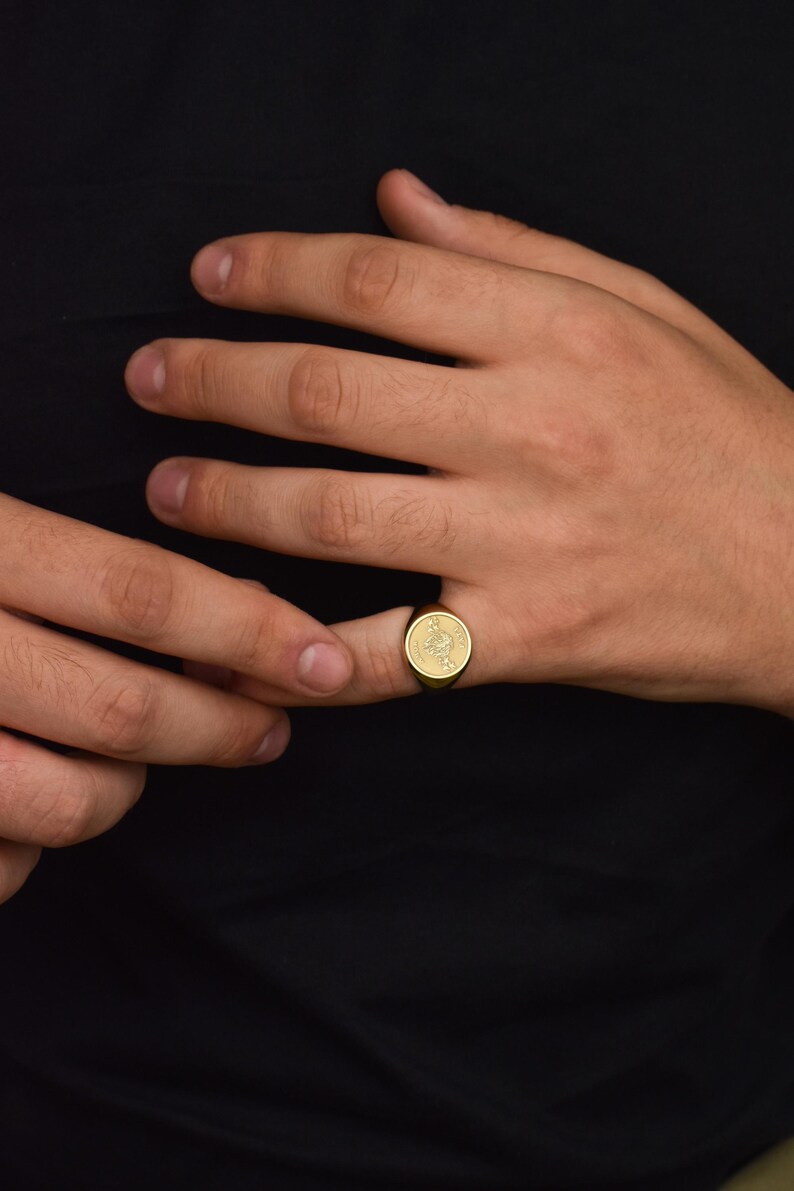 K&ouml;nnte beinhalten: Ein goldener Siegelring mit einem detaillierten Design auf der Vorderseite.