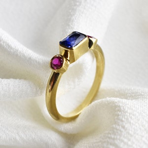 Peut inclure: Une bague en or avec une pierre rectangulaire bleue et deux petites pierres rondes roses.