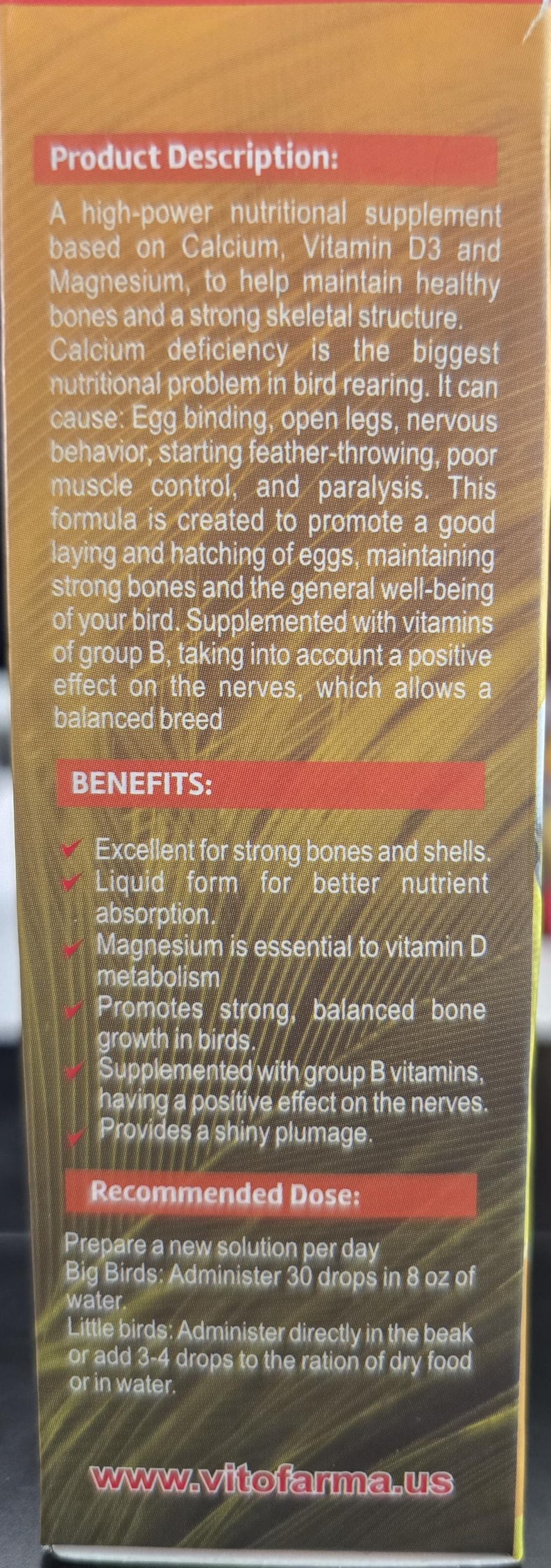May include: A product description on a brown and gold box for a nutritional supplement for birds. The text highlights benefits like strong bones, better nutrient absorption, and shiny plumage. The recommended dose is also included.